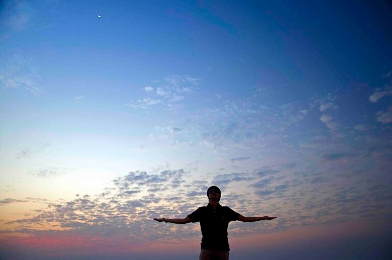 Silhouette of a man with open arms against a vibrant evening sky, symbolizing limitless possibilities.