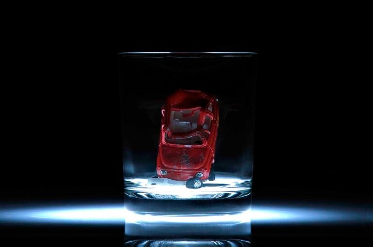 A symbolic photograph showing a red toy car placed inside a glass, conveying the message “Your drink is over… so are you” — highlighting the dangers of drinking and driving.