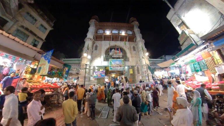 Buland Darwaza at Sarwar Sharif Dargah, Ajmer — exterior night view with devotees and city lights.
