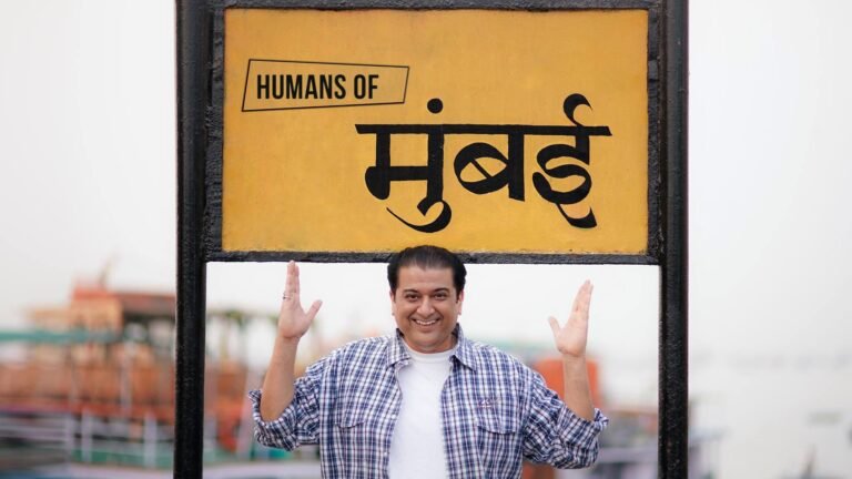 Humayunn Peerzaada smiling in front of a yellow ‘Humans of Mumbai’ board, symbolizing the city’s vibrant stories and spirit.