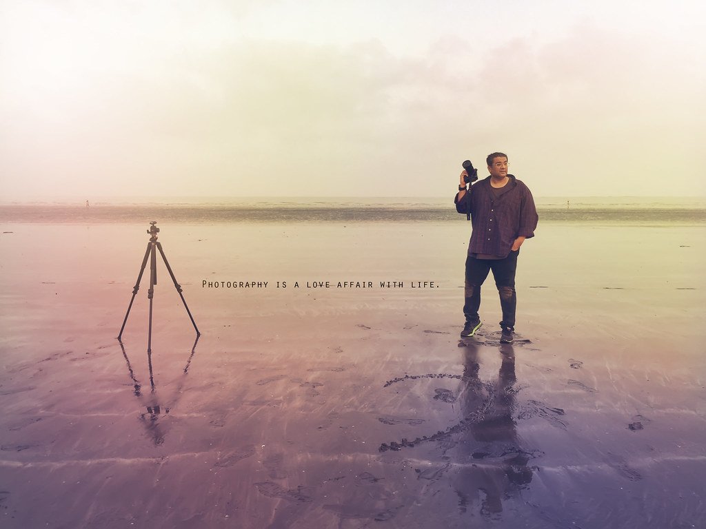 Humayunn Peerzaada standing with a tripod on the beach at sunset, symbolizing reflection, strength, and solitude.