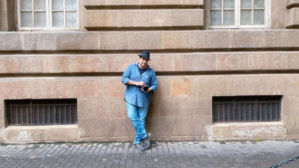 Humayun Peerzaada leaning against a heritage stone wall in Mumbai, holding a camera — a calm, creative portrait of a storyteller and visual artist.