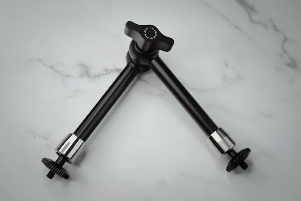 Black adjustable articulating magic arm placed on a marble background, used for mounting lights or monitors in professional creator setups.