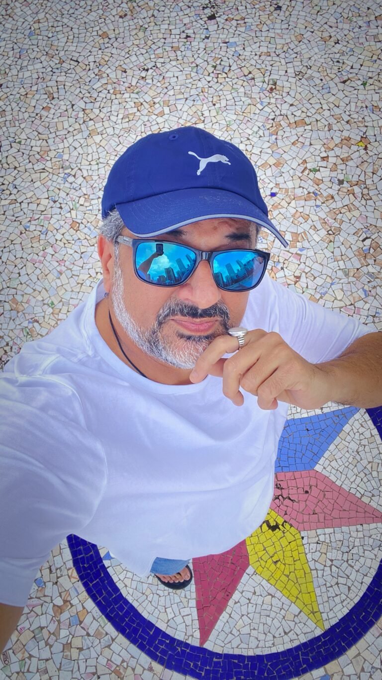Humayun wearing a white T-shirt, blue cap and blue sunglasses in a casual summer look