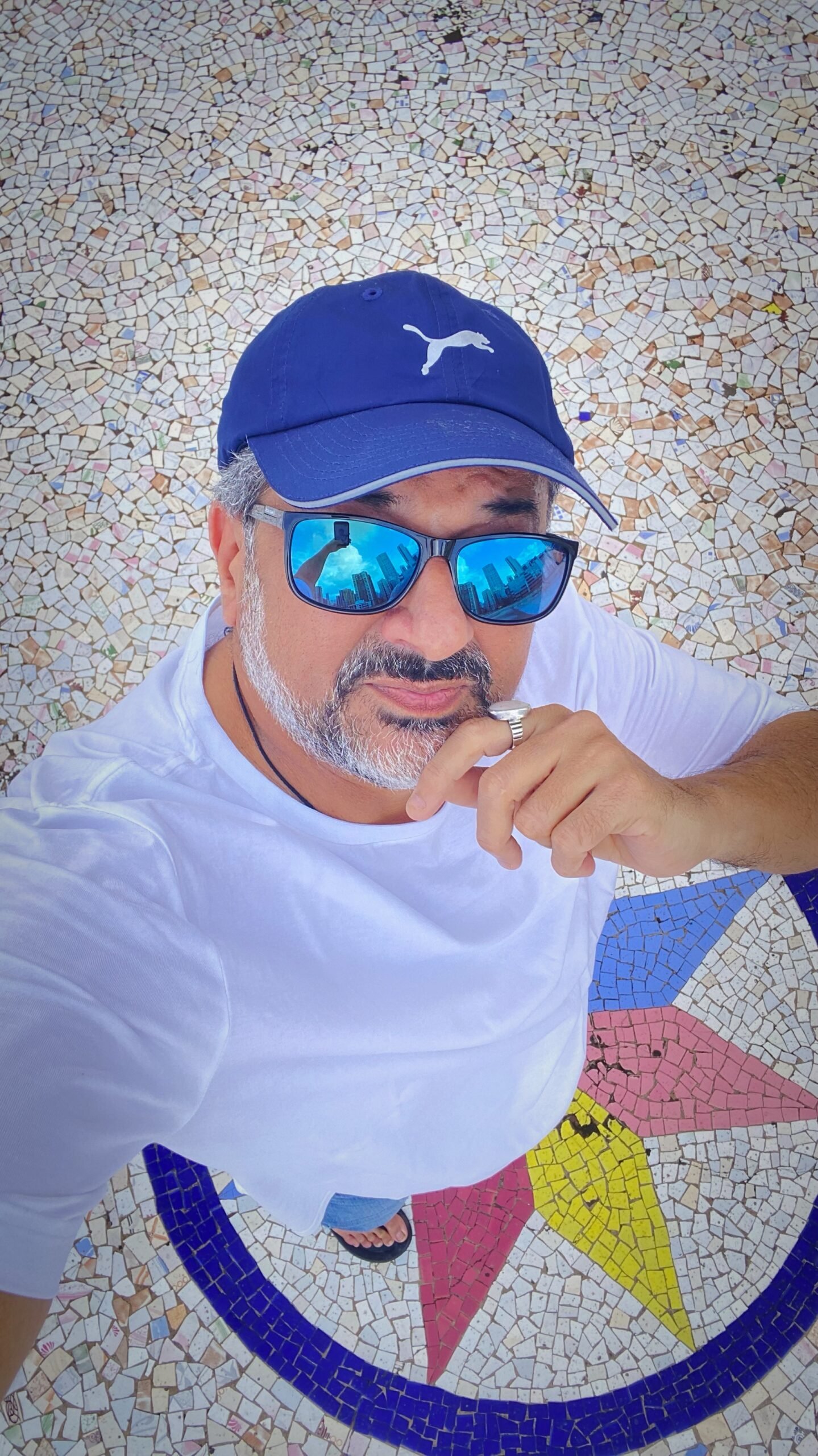 Humayun wearing a white T-shirt, blue cap and blue sunglasses in a casual summer look